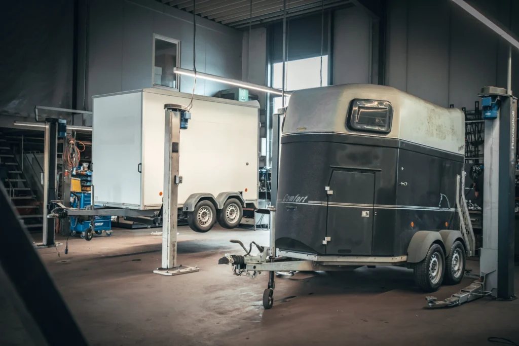 Zwei Anhänger in einer Werkstatt zur Wartung – geschlossener Kofferanhänger und Pferdeanhänger im professionellen Anhängerservice